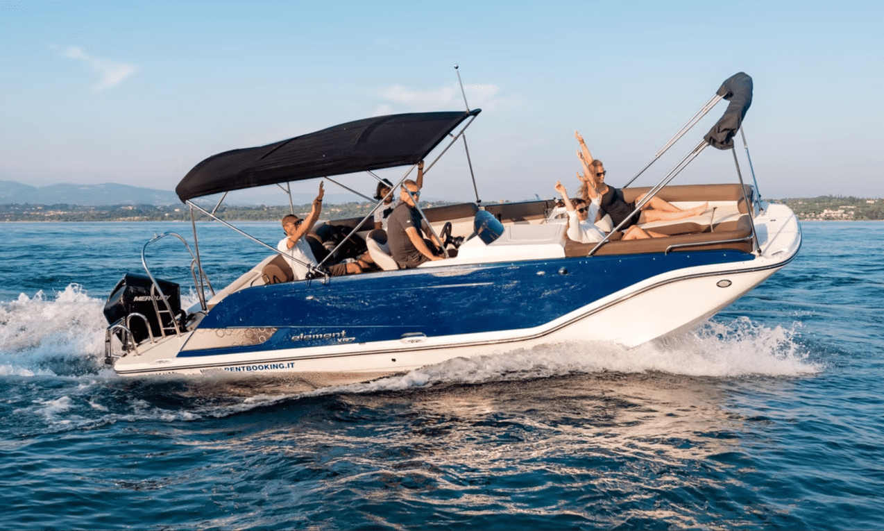 A blue and white motorboat with six people waving, creating a wake on the water.